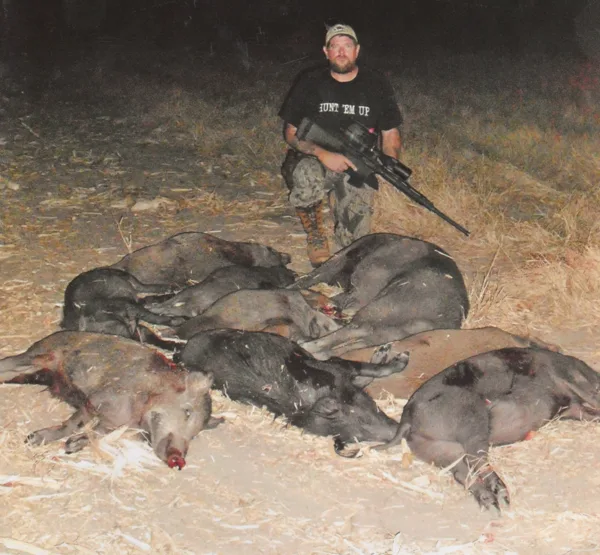 man with rifle next to pile of dead hogs