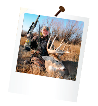hunter holding rifle and dead deer with large antlers out in a field