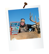 hunter holding big buck mineral formula bag and dead deer with large antlers in front of a barn