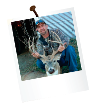 hunter in front of building holding antlers of a dead deer