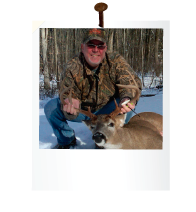 hunter in the snow and woods holding antlers of dead deer