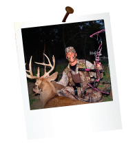 a hunter holding a bow next to a dead deer with large antlers